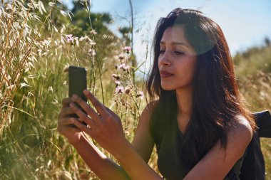 Doğada vahşi bitki örtüsüyle çevrili genç bir bayan mesajlaşıyor.