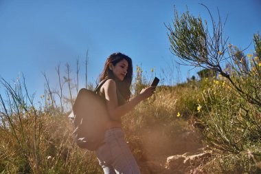 Güneşli bir günde yürüyüş yaparken meşgul genç bir bayan mesaj atıyor.