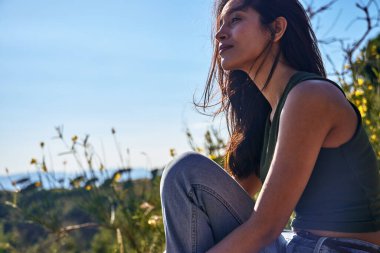 Kaygısız genç bir bayan doğada oturuyor rüzgar saçlarını usulca savuruyor.