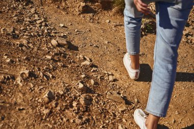 Genç bayan beyaz spor ayakkabı kullanarak çakıllı yolda yürüyor.