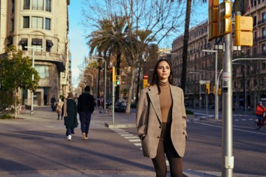 Taş suratlı bir kadın, elleri cebinde cadde boyunca yürüyor ve önüne bakıyor.
