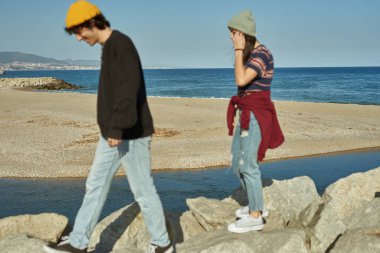 İki nişanlı genç, sahilde kayalıklarda yürüyor.