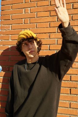 Yakışıklı beyaz adam, gün boyunca duvara yaslanırken yüzünü güneşten korumak için elini kullanıyor.