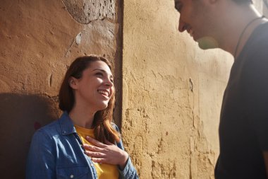 Genç bir kadın, genç bir adamla gülüyor. Şehirde bir caddede durup birbirlerine bakıyorlar.