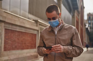 Orta yaşlı bir adam dışarıda duruyor. Mesajlaşırken iki eliyle telefonu tutuyor.