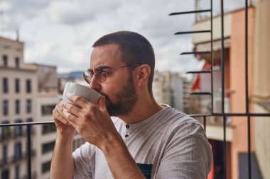 Orta yaşlı bir adam dışarıda balkonda içki içiyor.