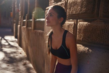 Güzel, siyah saçlı bir kadın, şehir caddesinde tuğladan bir duvara yaslanıyor. İnsanlar hafifçe öne doğru eğiliyor.