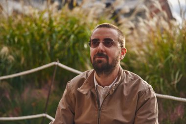 Soğuk, orta yaşlı bir adam derin düşüncelere dalmış, etrafı yabani otlar ve buğdaylarla çevrili.