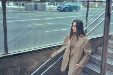 Ciddi bir kadın tek eliyle korkuluklara tutunarak merdivenlerden aşağı iniyor.