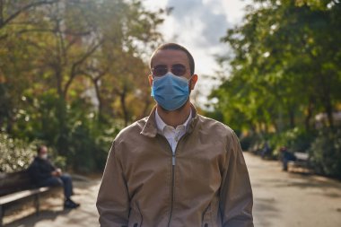 Sağlam orta yaşlı bir adam dışarıda dikiliyor ve doğrudan kameraya bakıyor.