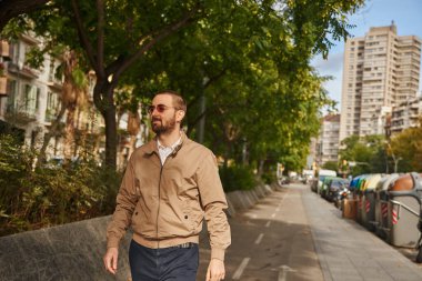 Dalmış bir adam kaldırımda yürüyor, kolları yanda.