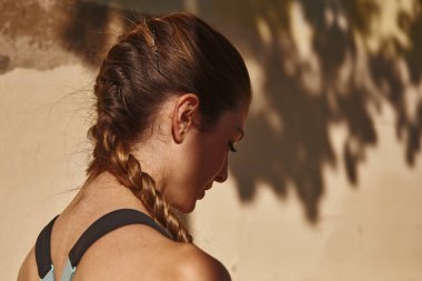 Ağaç dalları şehrin duvarına gölge düşürürken genç bir kadın aşağı bakıyor.