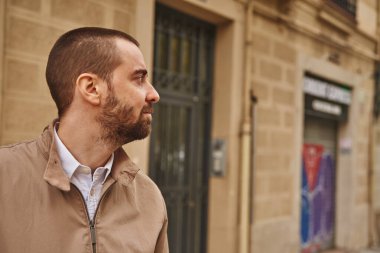 Binanın yanında durup yan tarafa bakan zahmetsiz bir adam.