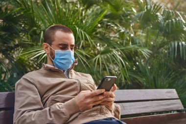 Orta yaşlı bir adam oturur ve mesajlaşırken arkasına yaslanır ve doğrudan telefonuna bakar.