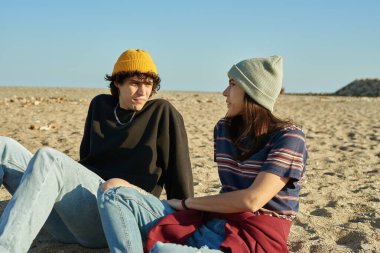 Çekici genç beyaz çift gün boyunca kumsalda dinlenirken sohbet ediyorlar.