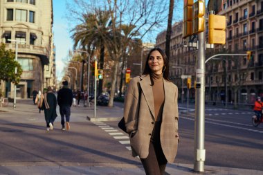 Caddede dikilip, uzaklara bakan neşeli bir kadın.