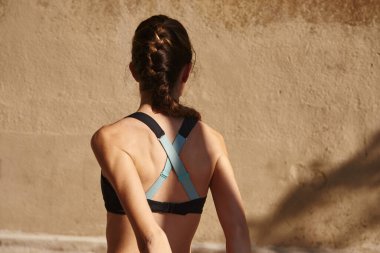 Sırtı kameraya dönük genç bir kadın kollarını arkaya uzatıyor.