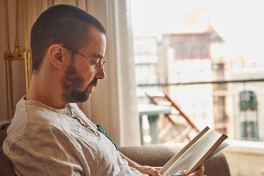 Orta yaşlı bir adam rahatça otururken kitap okuyor.