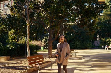 Memnun bir bayan, elleri ceketinin cebinde parkta geziniyor.