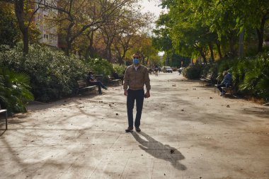 Dışarıda ağaçlar, binalar ve insanlarla çevrili asfalt bir yolda duran düz bir adamın vücut portresi.