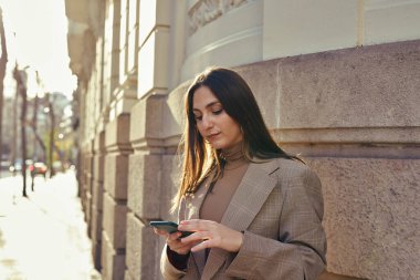 Binanın yanında duran dalgın kadın telefonuna bakarken mesaj atıyor.