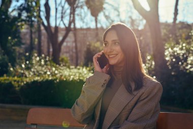 Parktaki bankta oturan neşeli bir bayan arıyor.