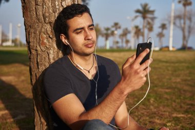 Çekici siyah saçlı genç adam cep telefonuna bakarken yüzüne bir cep telefonu tutuyor.