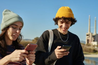 İki neşeli genç bir kumsalın yanında dururken telefonlarıyla meşgul oluyorlar.