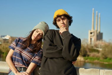 Yakışıklı bir adam gün boyunca sevgilisiyle köprüde dikilirken kameraya bakıyor.