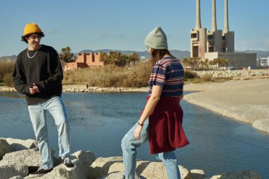 İki büyüleyici insan bir kumsalın kenarında birbirlerine bakan kayalıklarda duruyorlar.