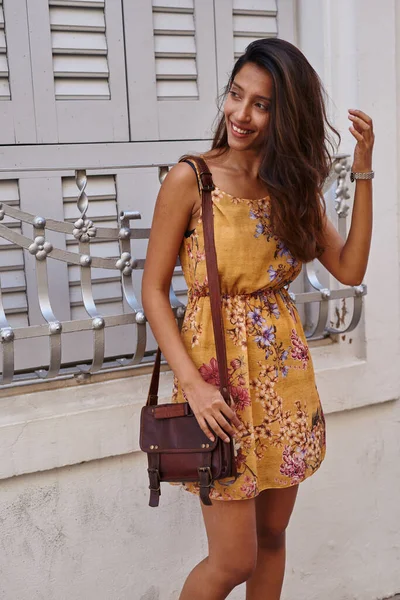 Playful lady happily gazing to side holding a sling bag and bending one knee