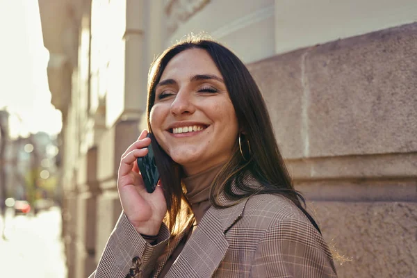 Bir binanın yanında beklerken telefonda gülümseyen mest olmuş kadın.