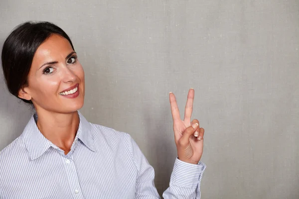 Mulher sorrindo e mostrando sinal de vitória — Fotografia de Stock