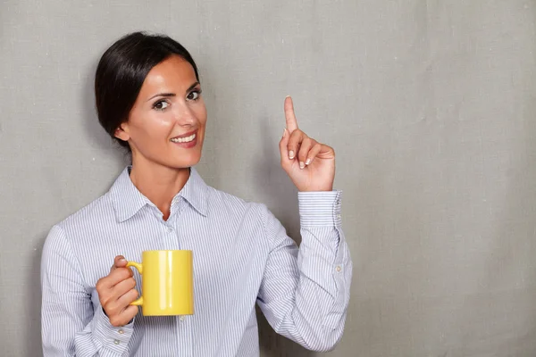 Smiling female with hot drink pointing up — Stock fotografie
