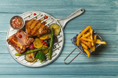 Pişmiş sebzeli pirzola ve kızarmış patatesler çelik ızgara tabağında ya da mavi bir kırsal masada pişmiş.