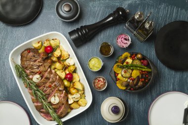 Sos ve süslemeli sığır güveci ile yemek masası, karabiber karıştırıcı ve farklı mezeler.