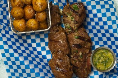 Çubukta sığır eti ve yanında da metal bir tepside kızarmış kreole patatesler var.