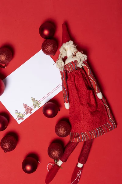 Blank Christmas card with rag doll on red table with Christmas baubles scattered all around in shades of red