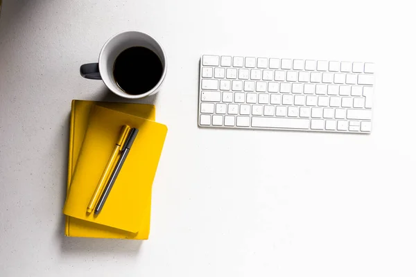 究極の灰色のコーヒーマグカップの横に白いキーボードと今年の鉛筆の色と黄色のノートブックを照らす白いテーブル — ストック写真