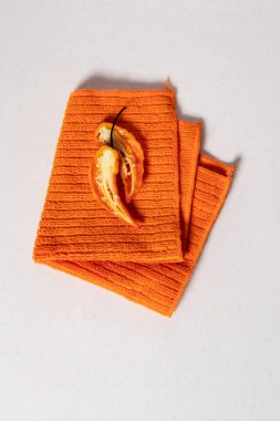 Portakal rengi dolma biber ikiye bölünmüş, ortasında çekirdekler, turuncu desenli mutfak havlusunda katlanmış.