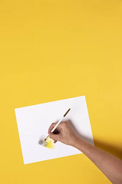 Hand with brush painting gray and yellow gradient with watercolor pencils on a yellow desk