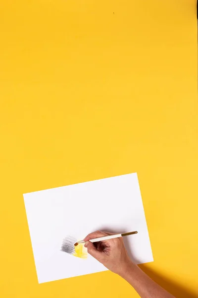 Hand with brush painting gray and yellow gradient with watercolor pencils on a yellow desk