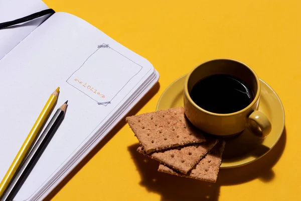 年の目標を計画するためのツールと弾丸ジャーナルノートブックの横にコーヒーとクッキーと黄色のカップ ストック写真