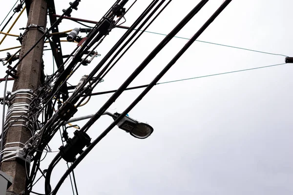 Silhouette of the electricity cables for the light of the houses of a city with a cloudy and gray sky