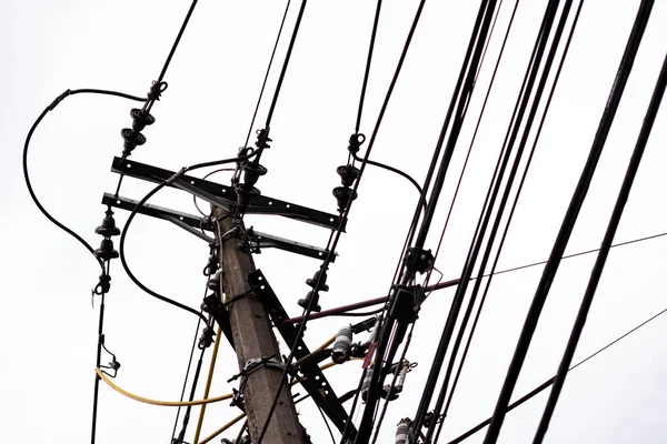 Silhouette of the electricity cables for the light of the houses of a city with a cloudy and gray sky