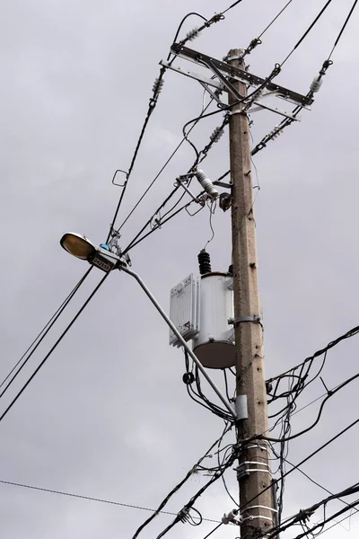 Silhouette of the electricity cables for the light of the houses of a city with a cloudy and gray sky