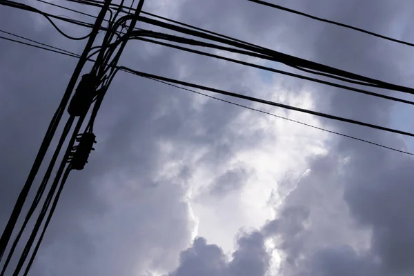 Silhouette of the electricity cables for the light of the houses of a city with a cloudy and gray sky