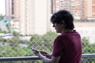 Hayvan güvenlik ağıyla balkonda yeşil manzaraya bakan bir adam var.