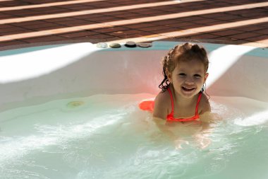 Turuncu mayo giyen küçük kız jakuzide suyun tadını çıkartıyor ve yüzmeyi öğreniyor.