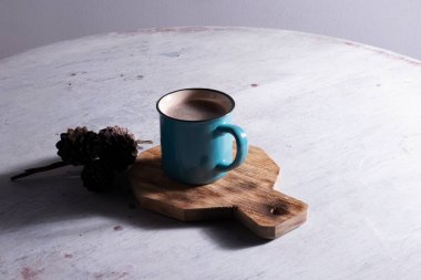 Mavi kupa beyaz masada dekupaj ve çam kozalakları eşliğinde ahşap masa